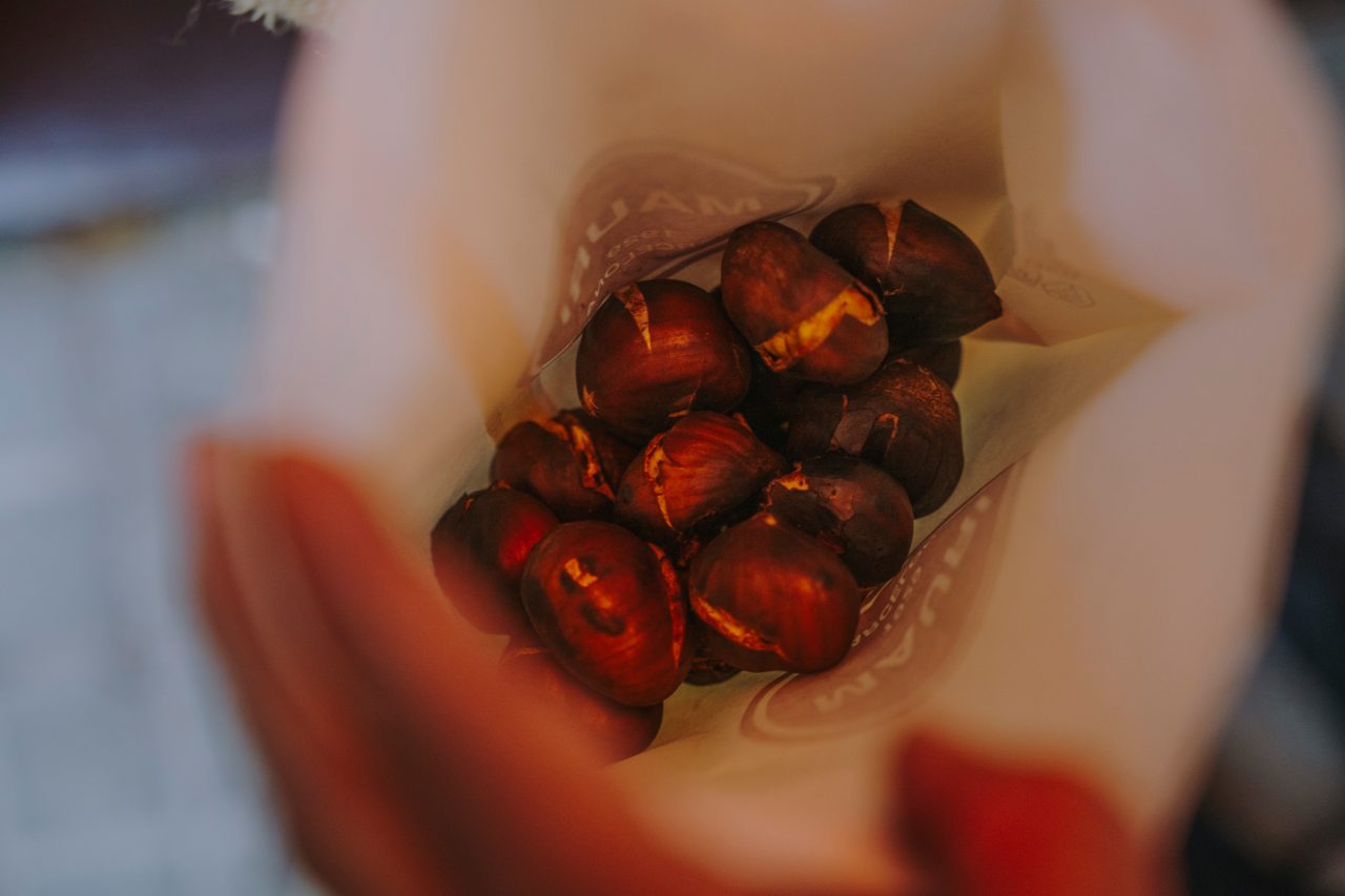Close-up of a paper cone of roasted chestnuts held in someone’s hands.