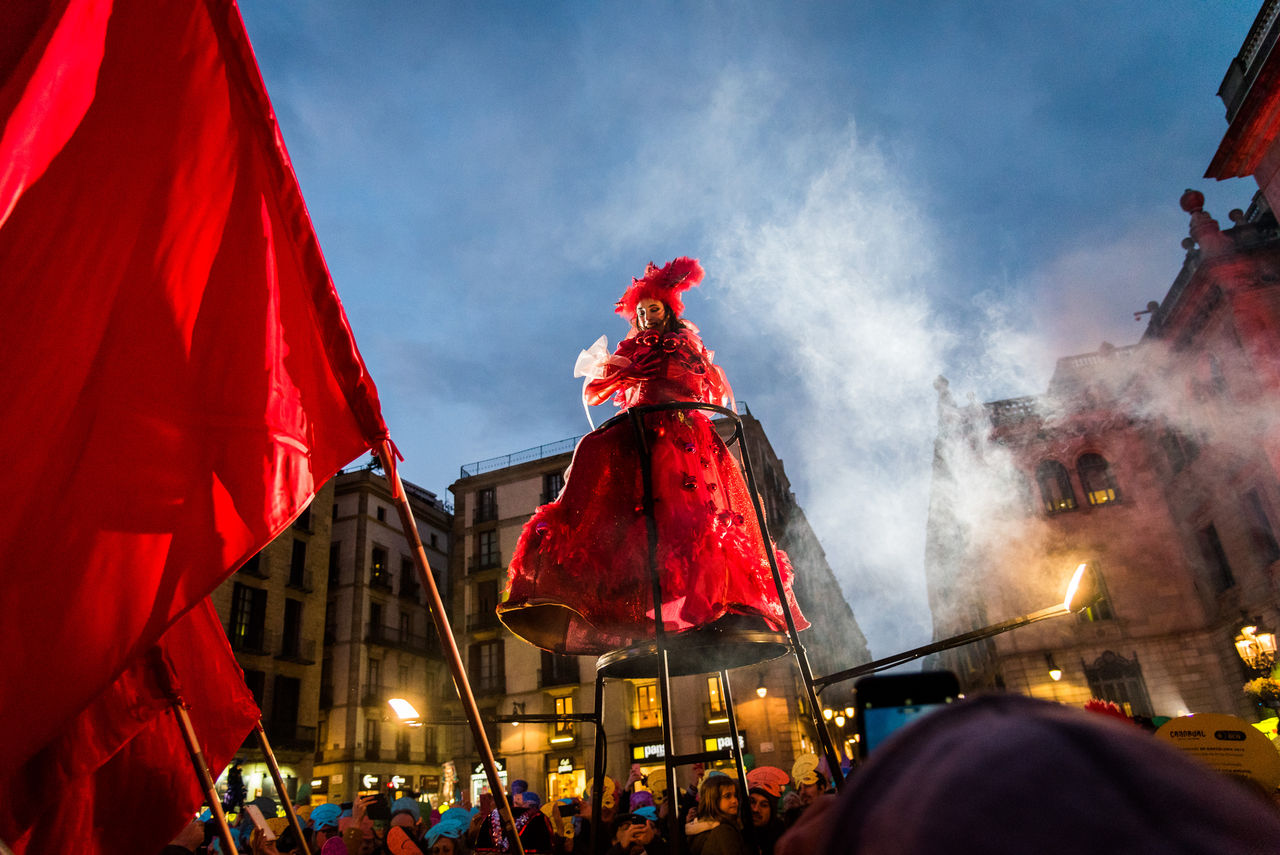 Noia pujada en una estructura vestida de vermell amb molta gent al voltan i banderes vermelles