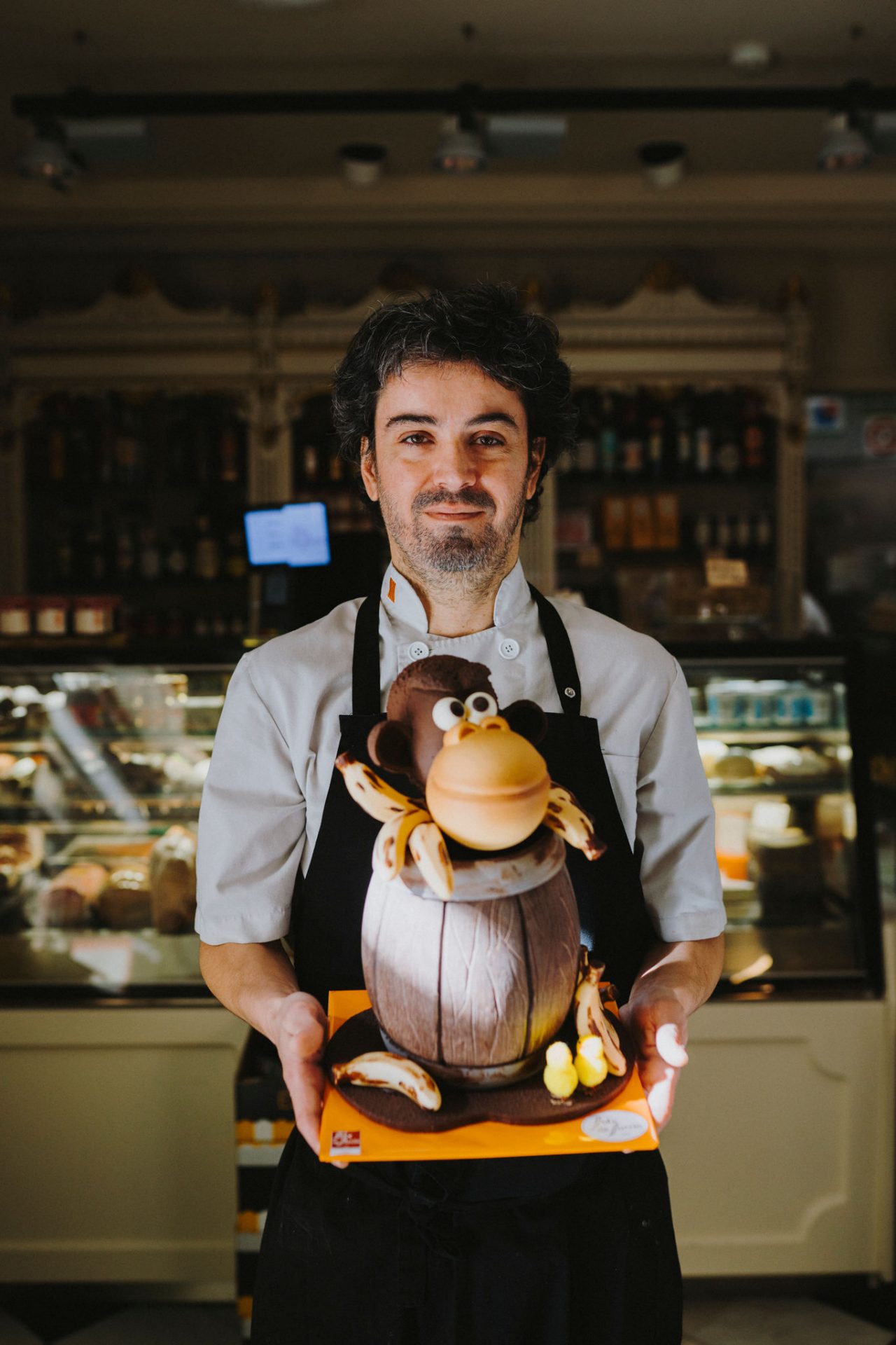 Pastisser amb una Mona de Chocolata a les mans i de fons l´interior de  la pastisseria del Foix de Sarrià