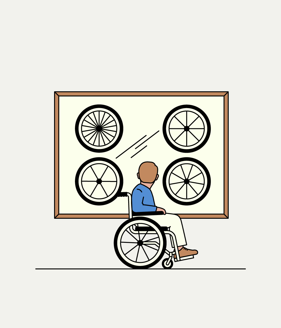 Persona in sedia a rotelle che osserva un’esposizione di ruote in uno spazio accessibile.