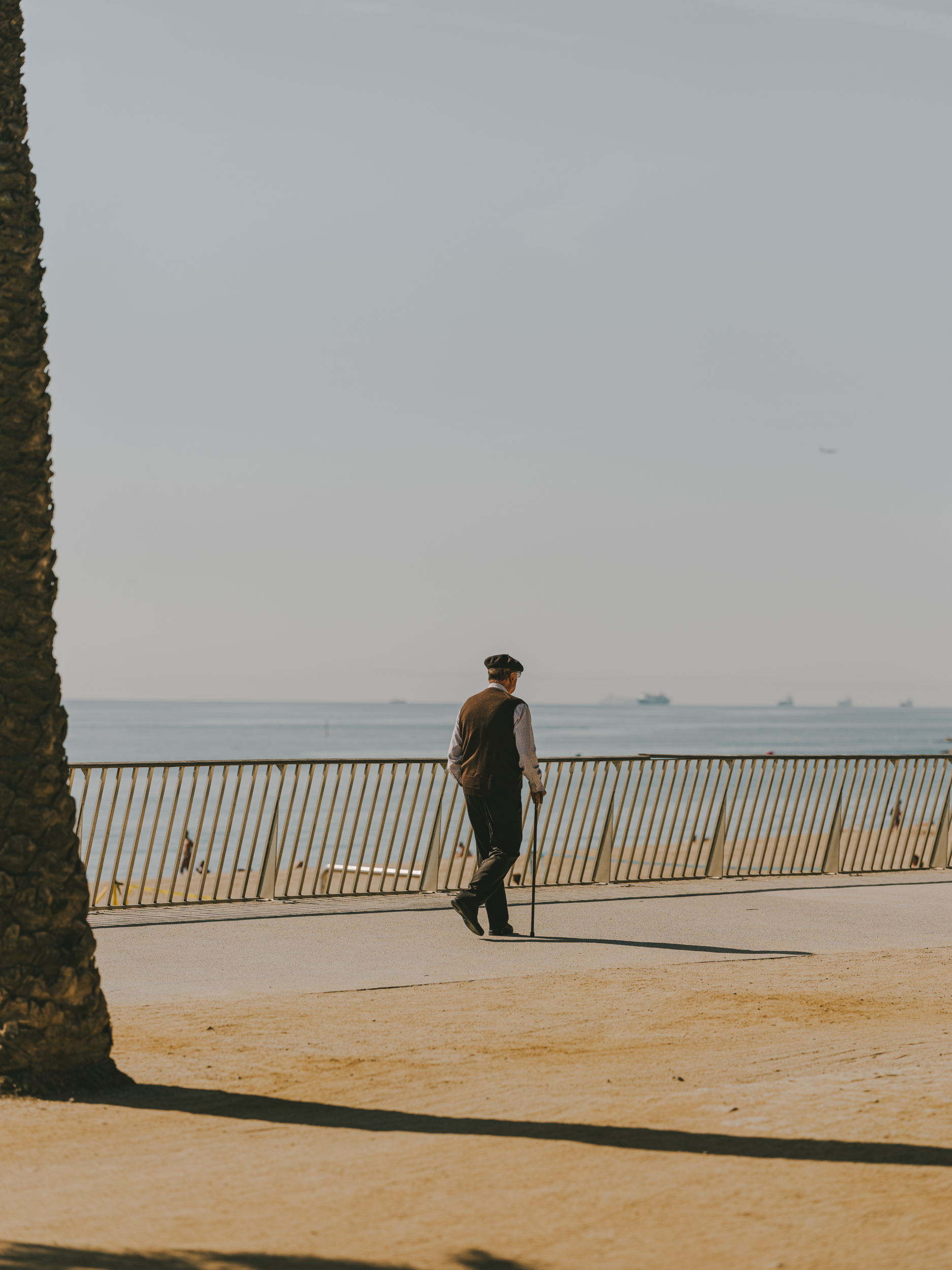 A man wearing a beret walks along the seafront promenade.