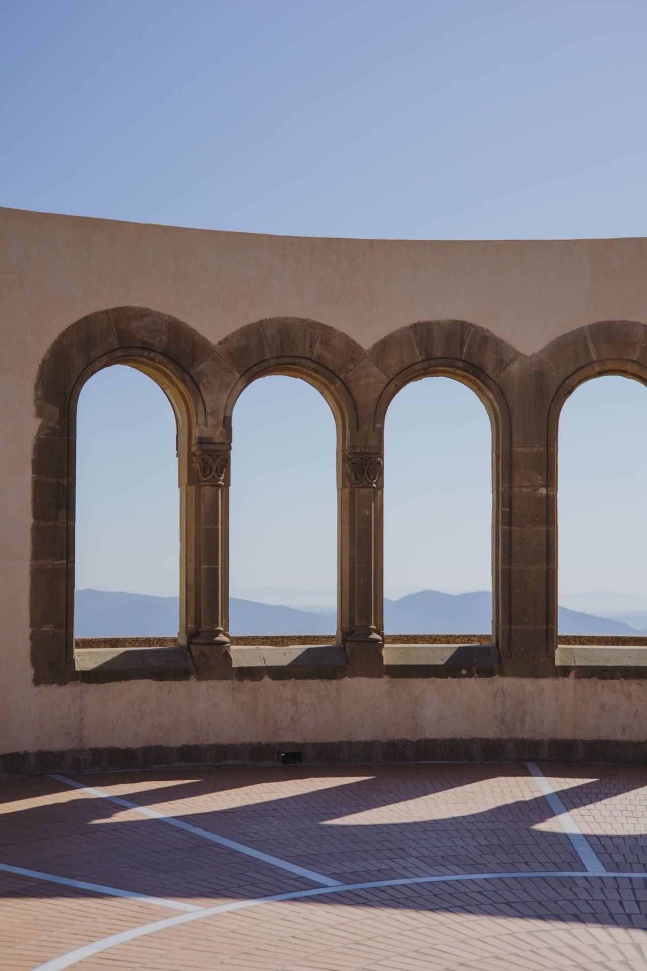 Stone arches overlooking the mountains from a viewpoint, with clear light and strong shadows on the ground.