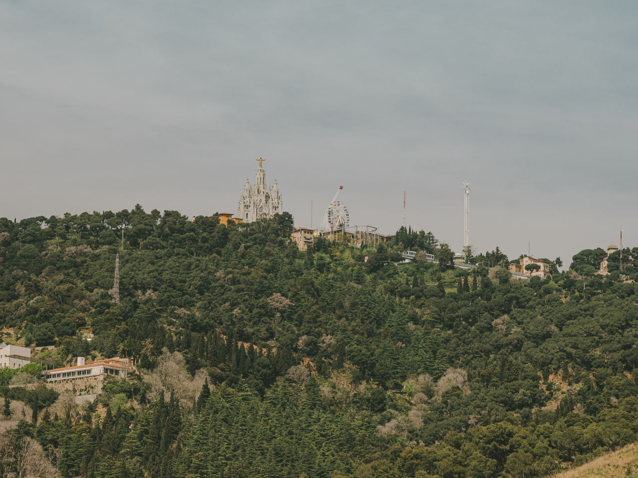 Vue de la montagne du Tibidabo avec le Temple Expiatori del Sagrat Cor, le parc d’attractions et une végétation abondante autour.