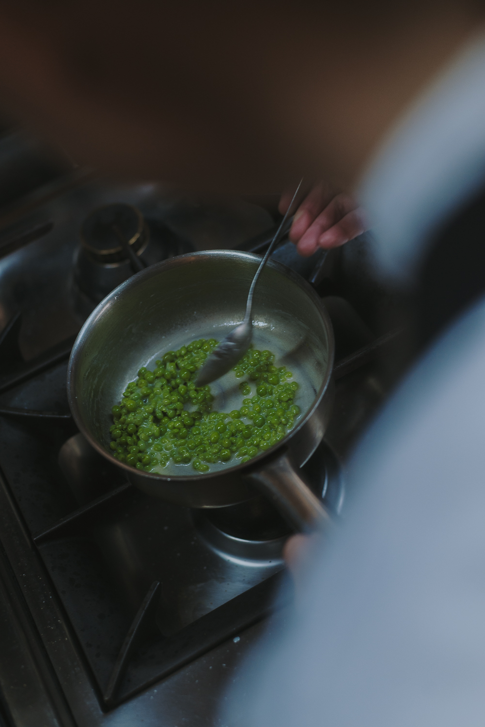 Casserole de petits pois verts cuisant sur le feu pendant qu’une personne les remue avec une cuillère dans une cuisine professionnelle.