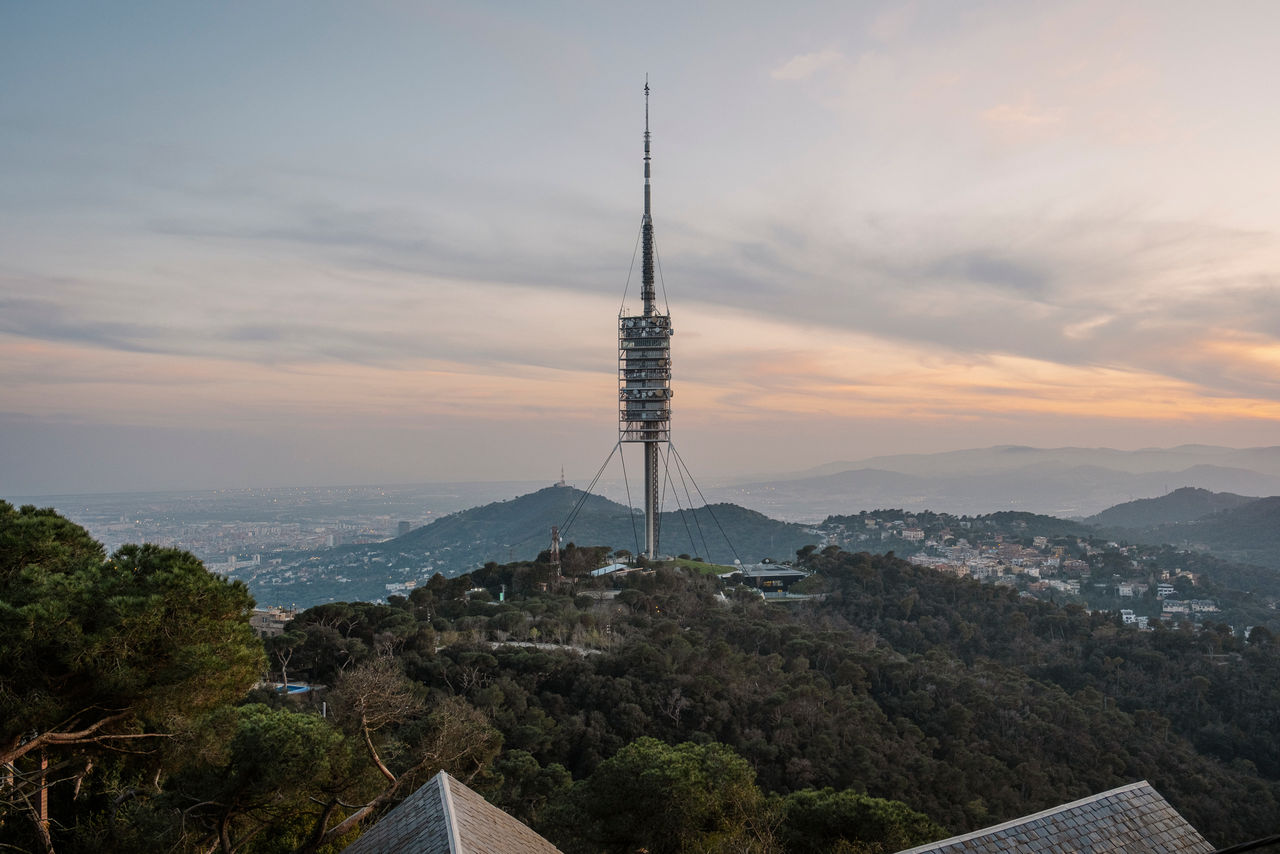 Vue du Tibidabo avec la tour de Collserola au centre, entourée de forêt, avec la ville de Barcelone en arrière-plan au coucher du soleil.