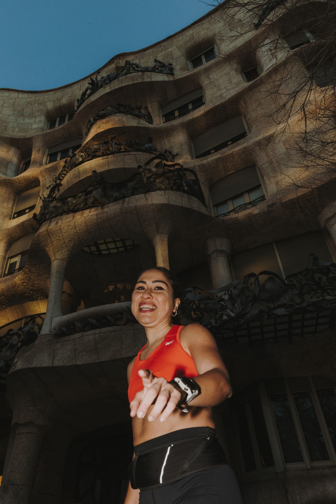 Une femme portant un top orange court devant la façade de La Pedrera.