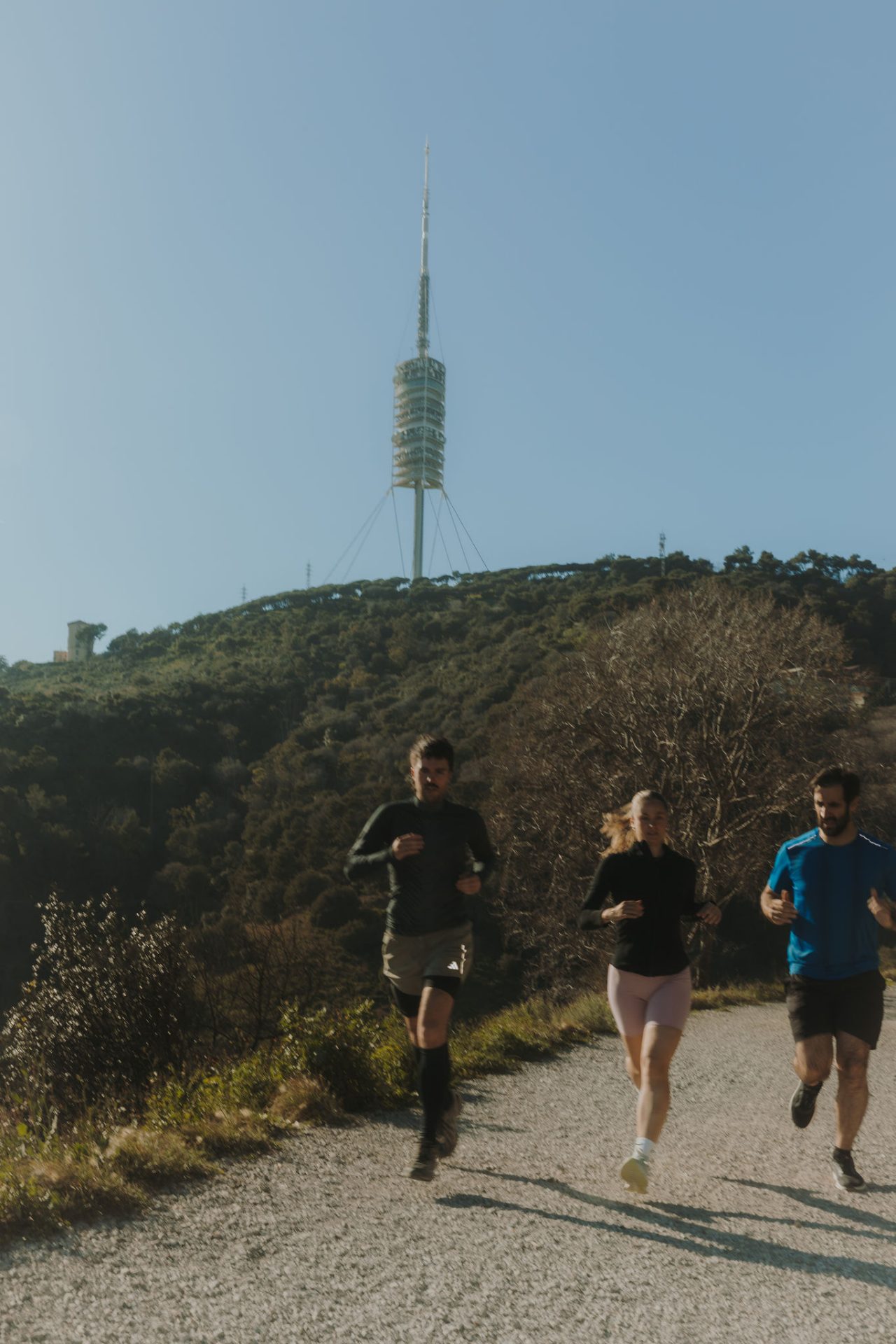 Tre persone corrono lungo un sentiero sterrato in un’area naturale, con la Torre di Collserola sullo sfondo.