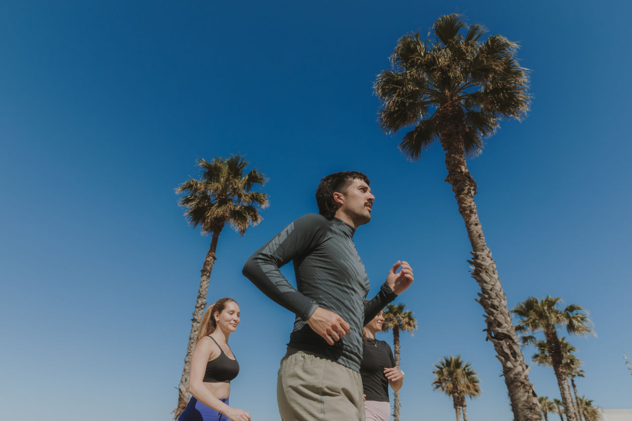 Due persone corrono tra le palme, con un cielo azzurro limpido sullo sfondo.