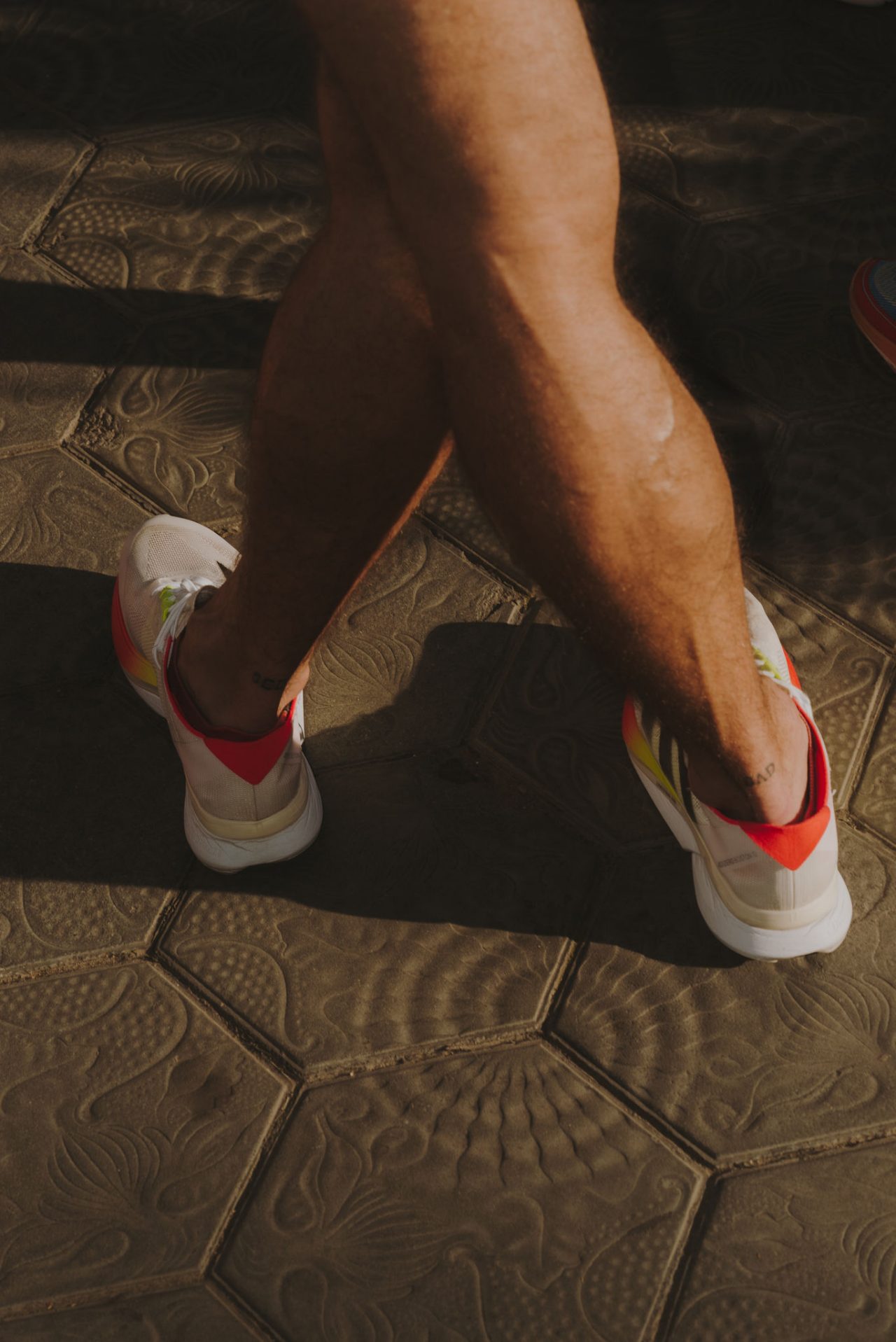 Primo piano delle gambe di una persona con scarpe da ginnastica bianche che cammina sulle piastrelle del passeig de Gràcia.